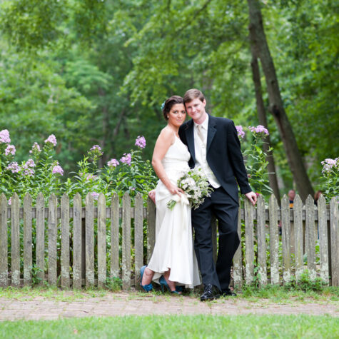bride and groom in park by fence and flowers