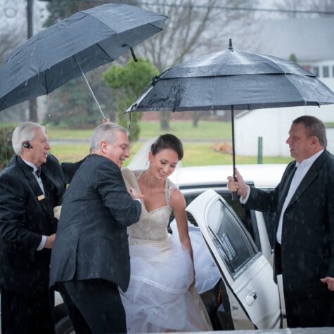 Bride getting out of limo lots of umbrellas
