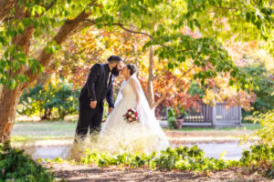 Bride and groom kissing in park under trees