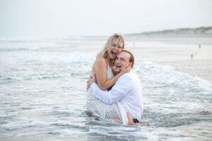 Bride and groom laughing sitting in clothes in ocean wet