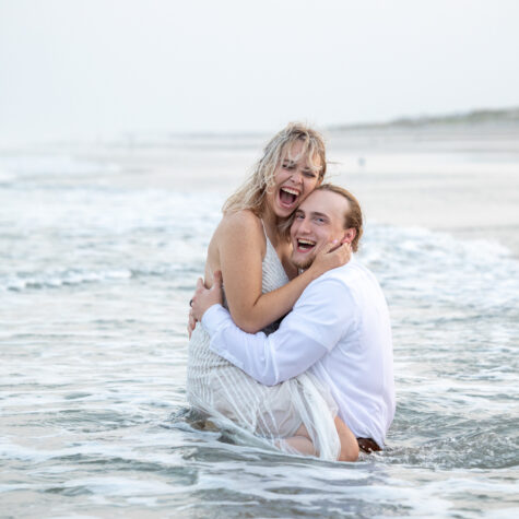 Bride and groom laughing sitting in clothes in ocean wet
