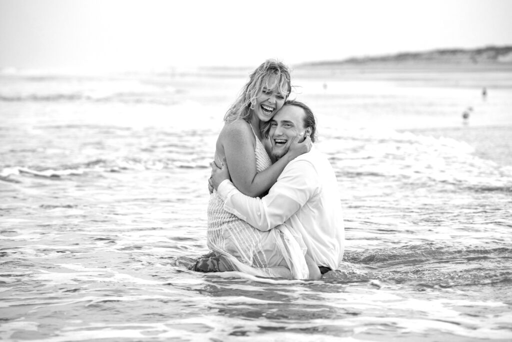 Fun couple in water on beach in clothes