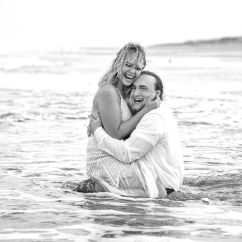 Fun couple in water on beach in clothes