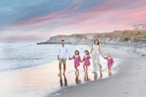 family walking on beach at sunset dressed in pink beige and white