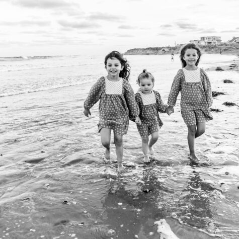 three little girls holding hands walking on beach