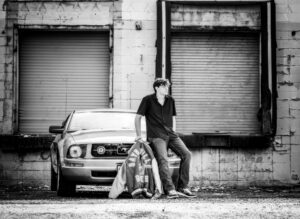 High school senior boy sitting on car with varsity jacket