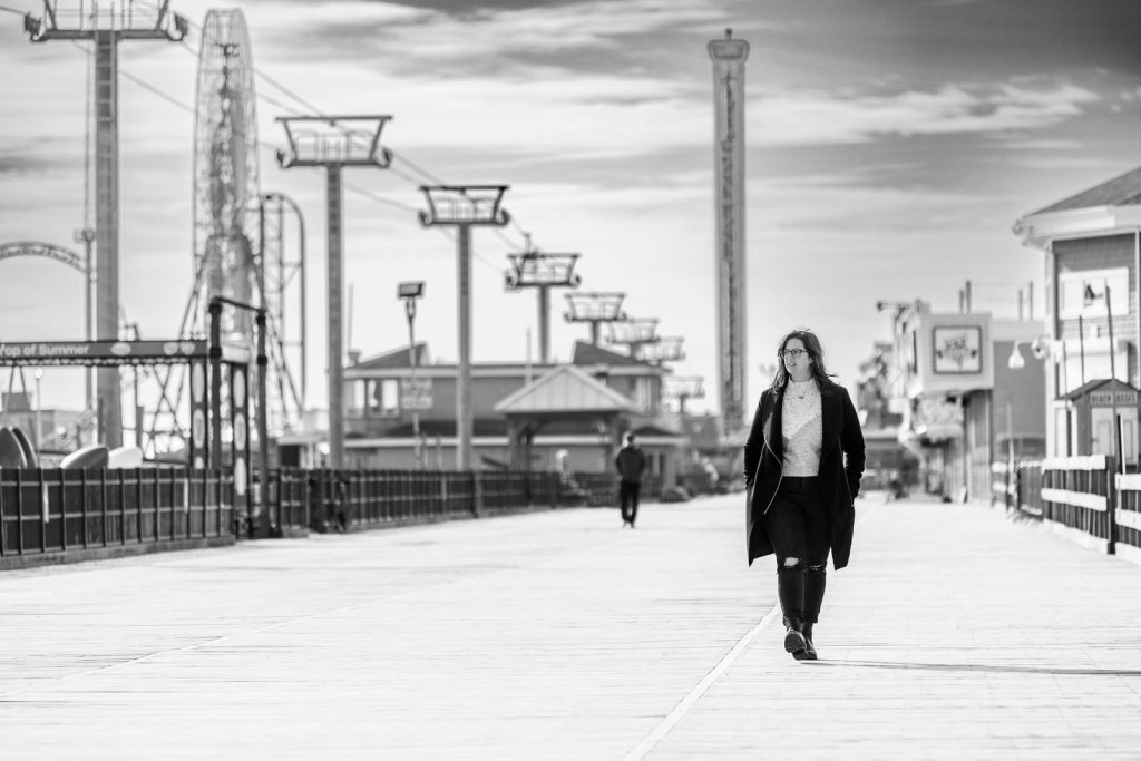 Black and white woman walking wearing long coat on boardwalk