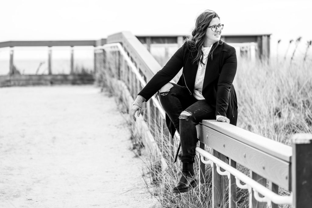 Black and white business coach sitting on beach path in winter in long flowing coat