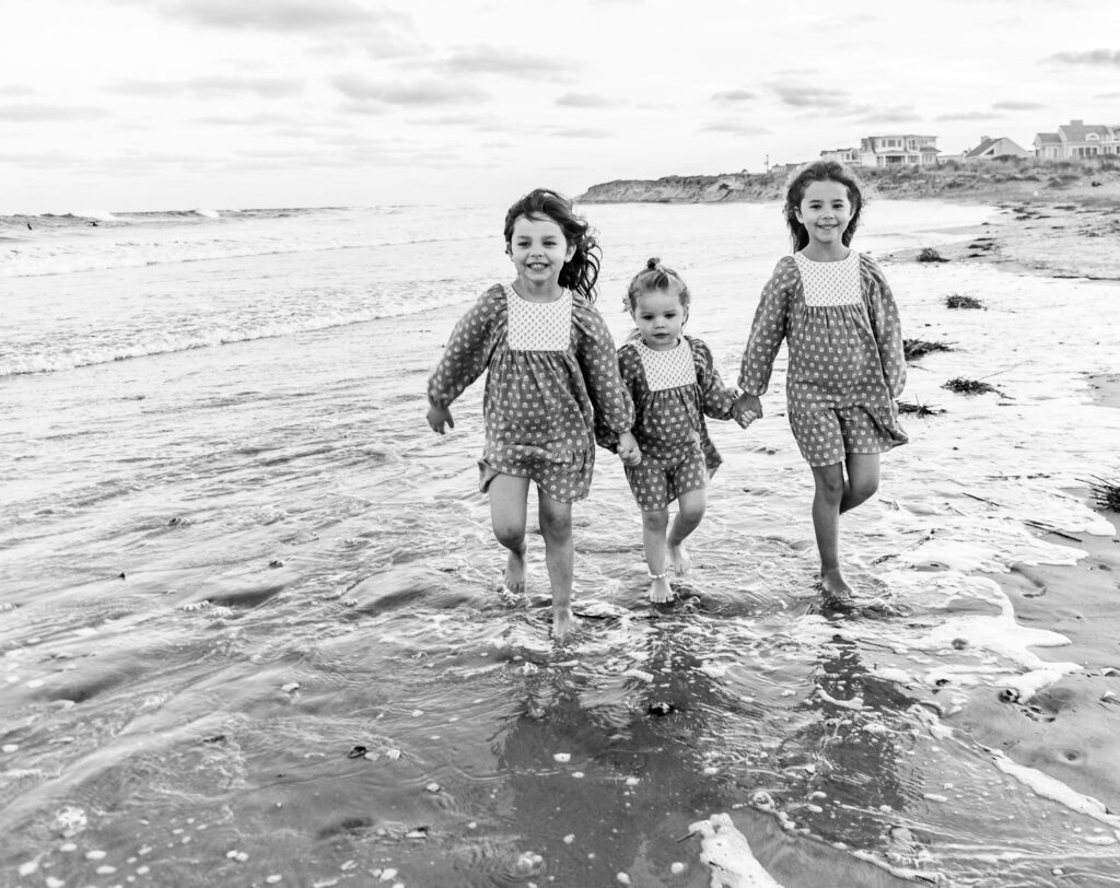 Three little girls holding hands running through beach water 
