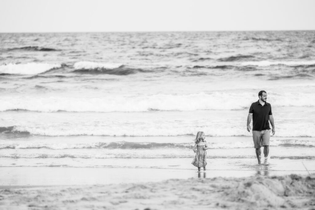 Dad and daughter on beach walking natural black and white 