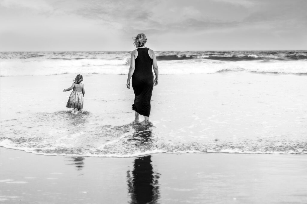 mom and daughter seen from behind walking into ocean water